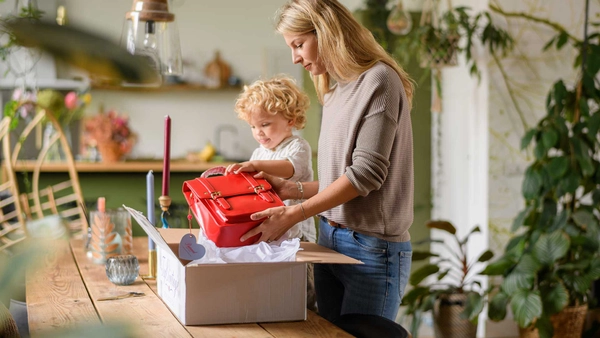 Vrouw en haar zoontje pakken samen een rode tas in een verzenddoos