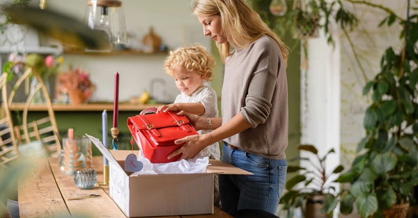 Vrouw en haar zoontje pakken samen een rode tas in een verzenddoos